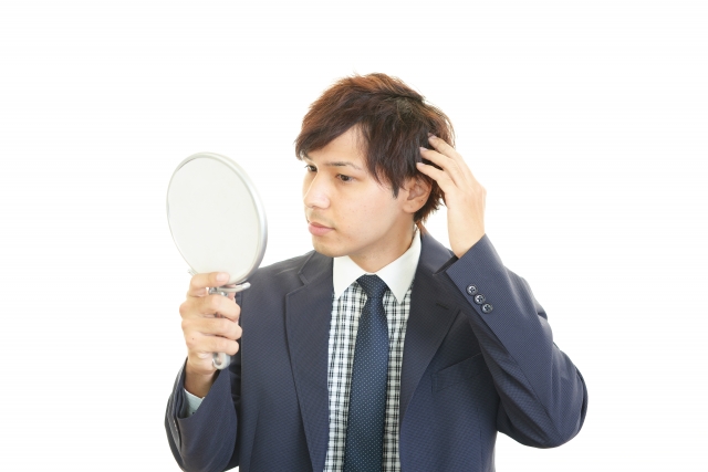 手鏡で自分の白髪を確認している男性